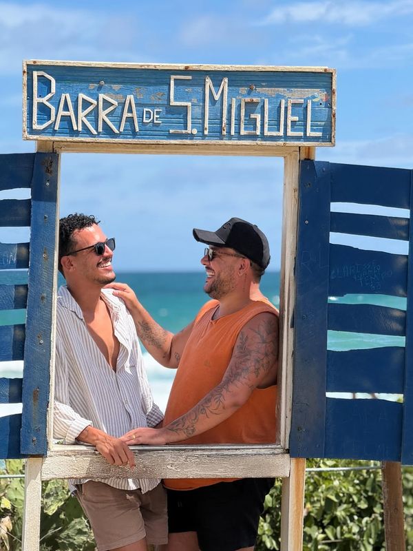 Casal rindo na moldura de Barra de São Miguel, com o mar ao fundo