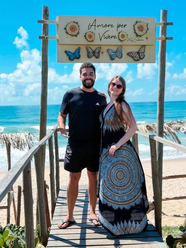 Casal sorrindo na passarela da praia, em frente ao mar